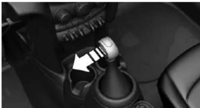 Close-up of a car gear shift lever mechanism with a white arrow pointing to the pivot point (no text or symbols visible)