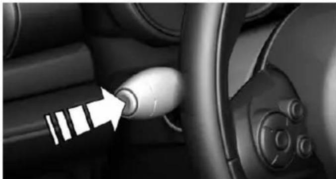 Close-up of a car interior showing a white arrow pointing to a button on the steering wheel (no text or symbols visible)