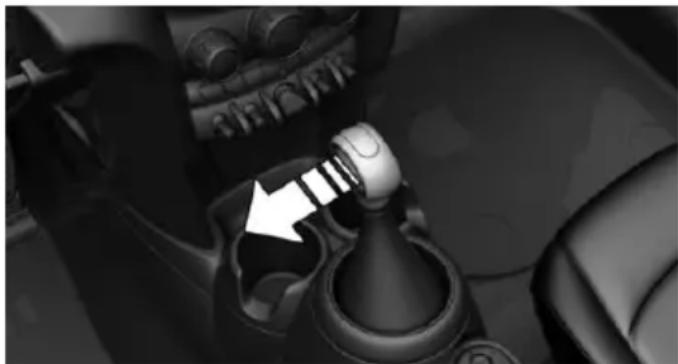 Close-up of a car gear shift lever mechanism with a white arrow pointing to the pivot point (no text or symbols visible)