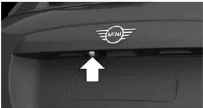 Close-up of a car's rear bumper with the Mini logo and an arrow pointing to a button (no text or symbols beyond the logo)