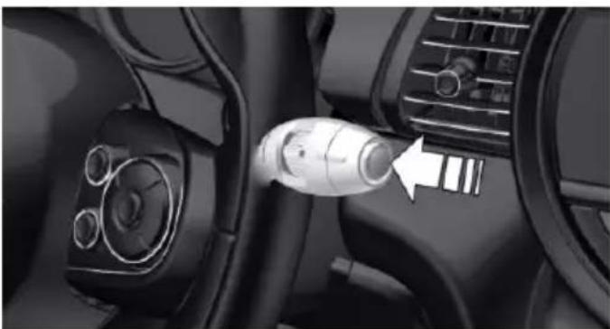 Close-up of a car interior showing a connector inserted into the dashboard with a white arrow pointing to it (no visible text or symbols)