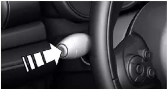 Close-up of a car interior showing a white arrow pointing to a button on the steering wheel (no text or symbols visible)