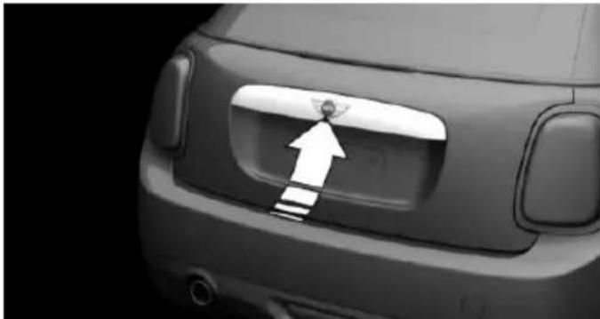 Close-up of a car's rear bumper with a white arrow pointing to a small object on the side (no text or symbols visible)
