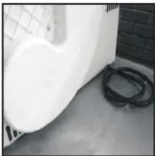 Exterior view of a white wall and a black hose on a concrete floor (no text or symbols visible)