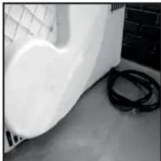 Close-up of a white plastic object with a coiled cable, placed on a dark surface near a grid-patterned wall (no text or symbols visible)