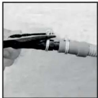 Close-up of a hand holding a thin wire with metal rings, partially connected to a coiled cable or pipe (no text or symbols visible)