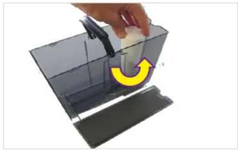 Hand placing a small object into a transparent container with a yellow curved arrow indicating rotation (no text or symbols).