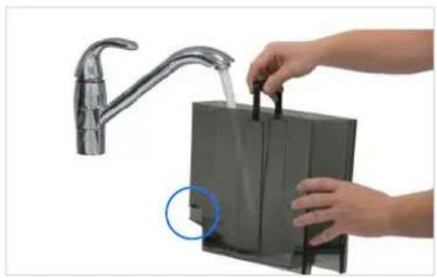 Person using a hand tool to clean or adjust a black appliance with a faucet (no text or symbols visible).
