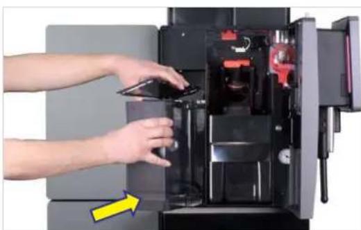 Person operating a 3D printer with open door and internal compartments, showing mechanical parts and a yellow arrow indicating motion (no text or symbols visible).
