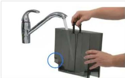 Person using a tool to clean or install a black rectangular device with a faucet (no text or symbols visible).