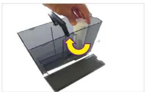 Hand placing a white object into a transparent container with a yellow curved arrow indicating rotation (no text or symbols).