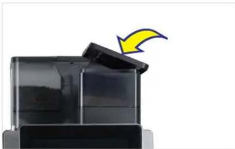 Close-up of a black plastic container with a yellow arrow pointing to its lid (no text or symbols visible).