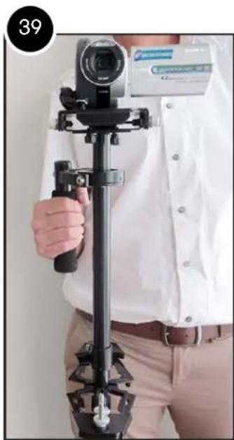 Person holding a camera setup with a tripod, wearing a white shirt and brown trousers (no visible text or symbols)