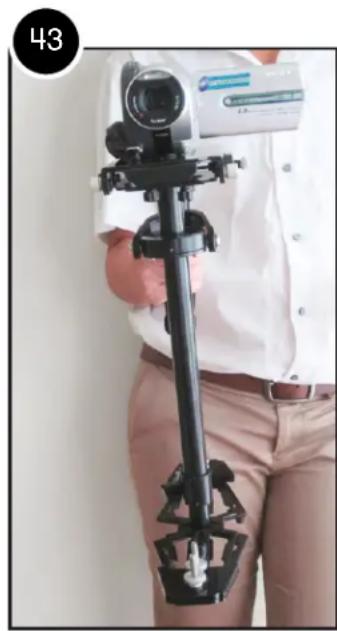Person holding a black tripod-mounted camera with a digital display (no visible text or symbols)