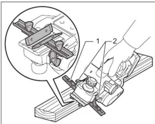 Technical diagram showing a hand operating a workbench with two views of a mechanical component, labeled 1 and 2.