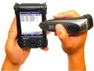 Person holding a smartphone displaying a financial data interface with text and a handheld device, likely for scanning or testing purposes.