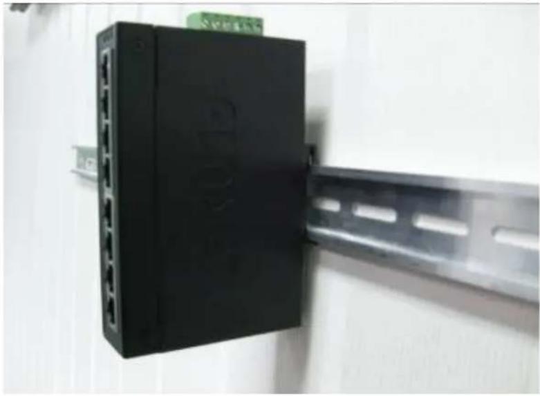 Close-up of a black electronic device mounted on a metal rail bar, no visible text or symbols