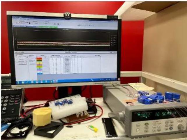 Lab setup with electronic testing equipment, a computer monitor displaying a waveform graph, and a digital oscilloscope labeled '10 SLC-10'.