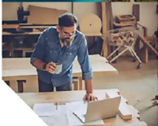 Man working at a wooden mill bench with a laptop and paper nearby (no visible text or symbols)