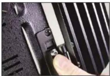 Close-up of a finger pressing down on a black mechanical component with a metallic clip (no visible text or symbols)