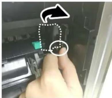 Hand pointing at a device with a green button and arrow icon, indicating a process or operation.
