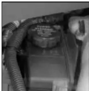 Close-up of a car engine bay with hoses and a central control panel (no visible text or symbols)