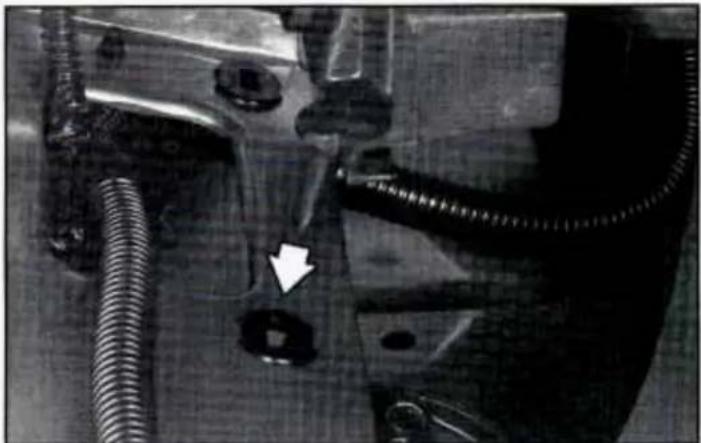 Close-up of a mechanical component with coiled tubing and a white arrow pointing to a hole (no visible text or symbols)