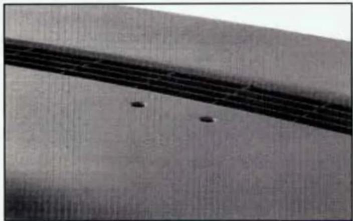 Close-up of a textured surface with parallel dark bands and small dark spots (no text or symbols visible)