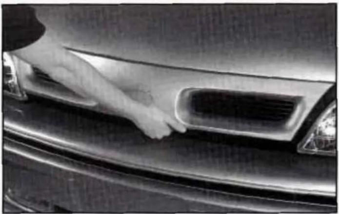 Close-up of a hand cleaning the dashboard of a car's front grille (no visible text or symbols)