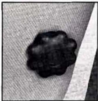 Close-up of a dark, irregularly shaped object on a textured gray background with a white diagonal stripe (no text or symbols visible)