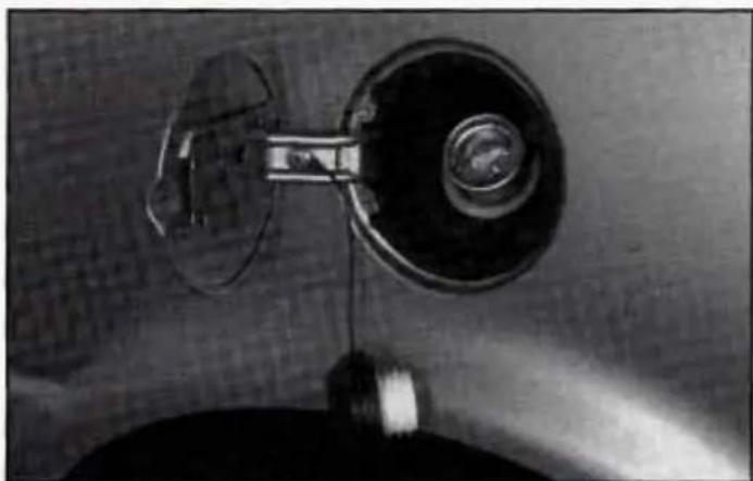 Close-up of a mechanical component with a circular head and attached rod, mounted on a surface (no visible text or symbols)