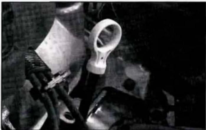 Black-and-white photo of mechanical components including a tool, clamped parts, and a plastic housing (no visible text or symbols)
