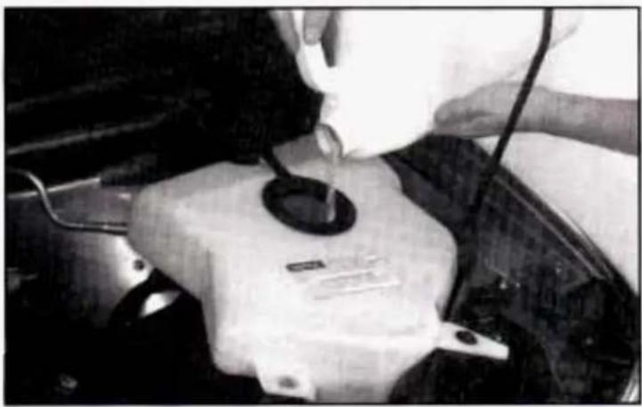 Person pouring liquid into a car engine compartment (no visible text or symbols)