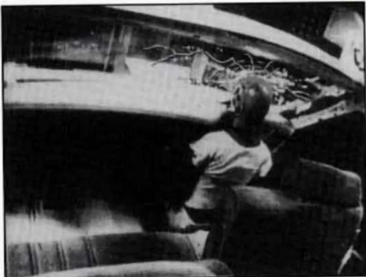 Black-and-white photo of a person sitting on a wooden boat hull, viewed from above (no visible text or symbols)