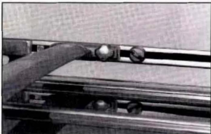Close-up of a hand operating a mechanical device with rollers and a wooden panel (no visible text or symbols)
