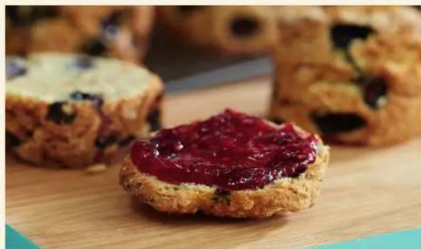Close-up of a baked sourdough with red jam against a blurred background of blueberry slices on a wooden surface.