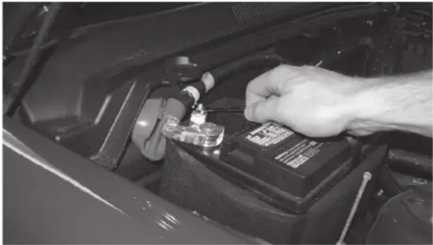 Close-up of a hand using a tool to adjust or install an electric vehicle battery on the engine compartment (no visible text or symbols)