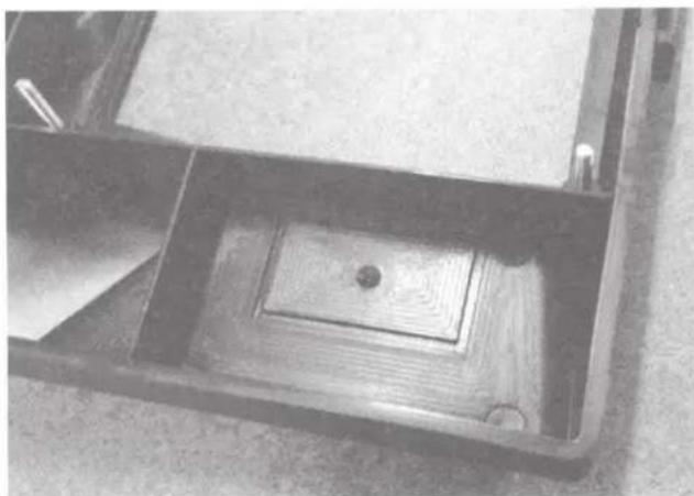 Interior view of a wooden table with a central square and two small items, no visible text or symbols