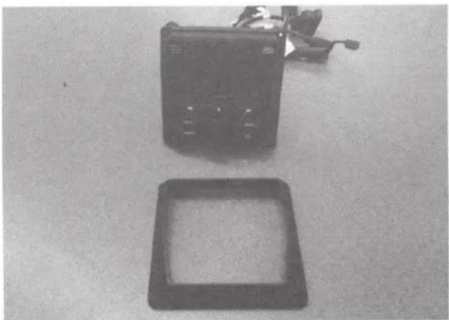 Black-and-white photo of a portable electronic device and a square frame on a plain surface (no text or symbols visible)