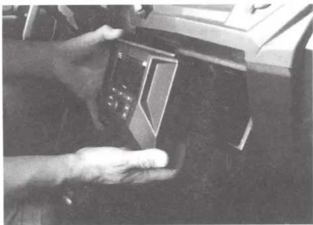 Close-up of a hand holding a small electronic device with a control panel, partially visible in the background (no text or symbols)