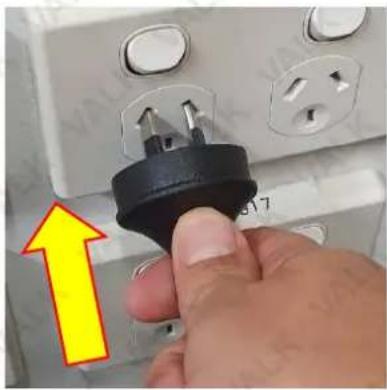 Close-up of a hand inserting a black plastic plug into an electrical socket (no text or symbols visible)