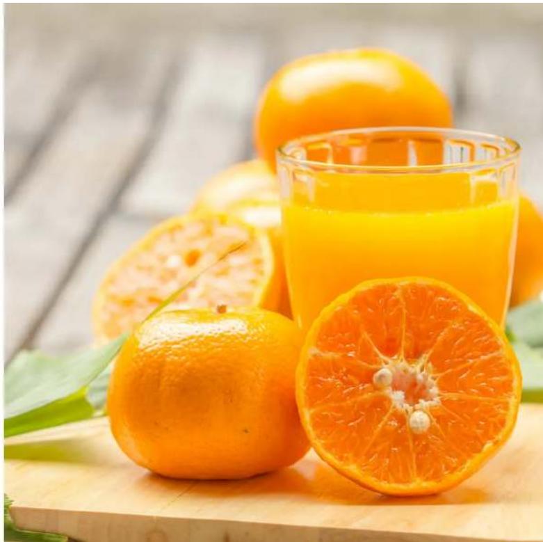 Freshly sliced oranges and a glass of juice on a wooden cutting board, with green leaves in the background (no text or symbols visible)