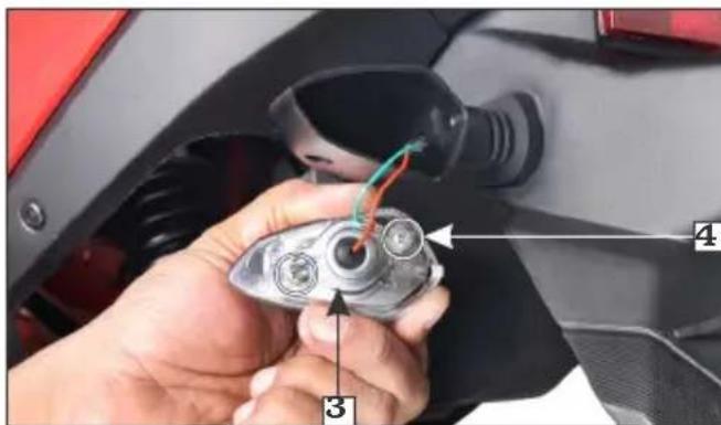 Close-up of a hand holding a car engine component with labeled parts 3 and 4, showing wiring and adjustment arrows.