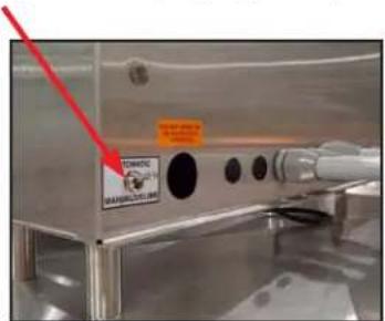 Photo of a stainless steel kitchen appliance with visible warning label and red arrow pointing to a black circular component.