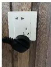 White electrical outlet mounted on a wooden wall with a black plastic bulb (no visible text or symbols)