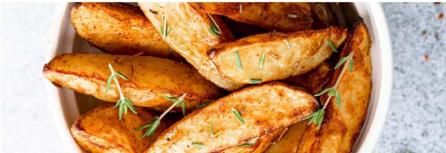 Close-up of golden-brown baked potatoes garnished with green rosemary, served in a white bowl (no text or symbols visible)