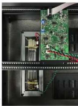 Interior view of an electronic equipment cabinet showing a green circuit board mounted on a rack, with wiring and components visible (no text or symbols)