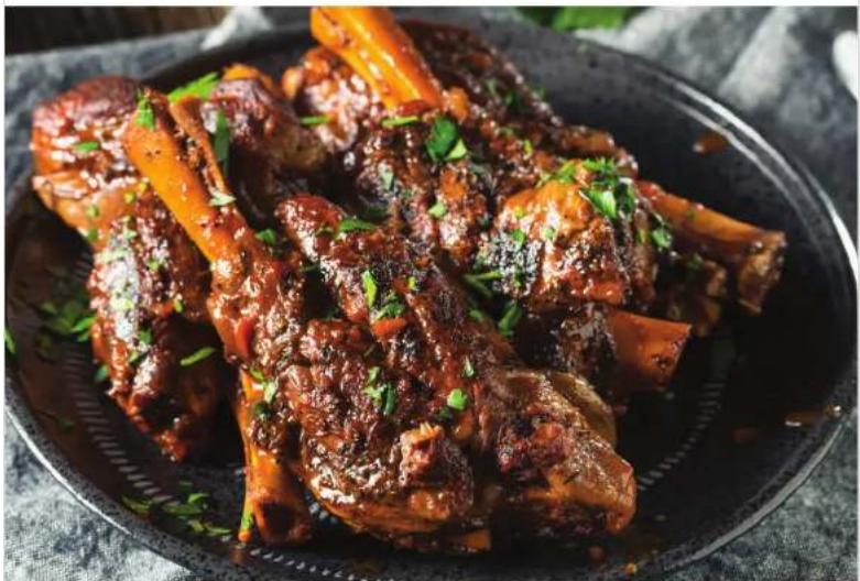 Close-up of braised pork ribs with green herbs on a dark plate (no text or symbols visible)