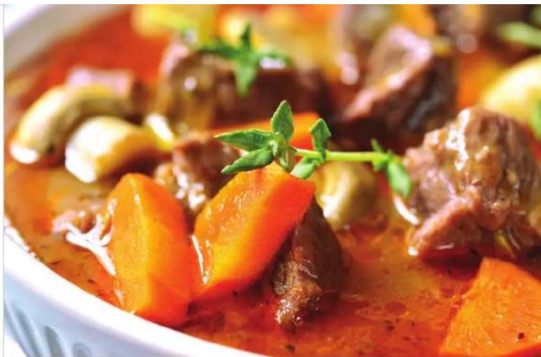 Close-up of a stewed meat dish with carrots and mushrooms, garnished with parsley (no text or symbols visible)