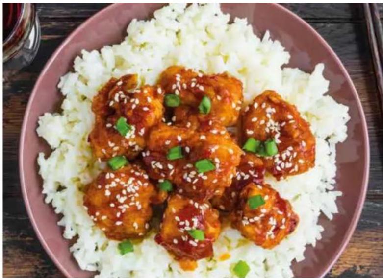 Plate of fried chicken wings topped with sesame seeds and green onions, served on a white rice dish.